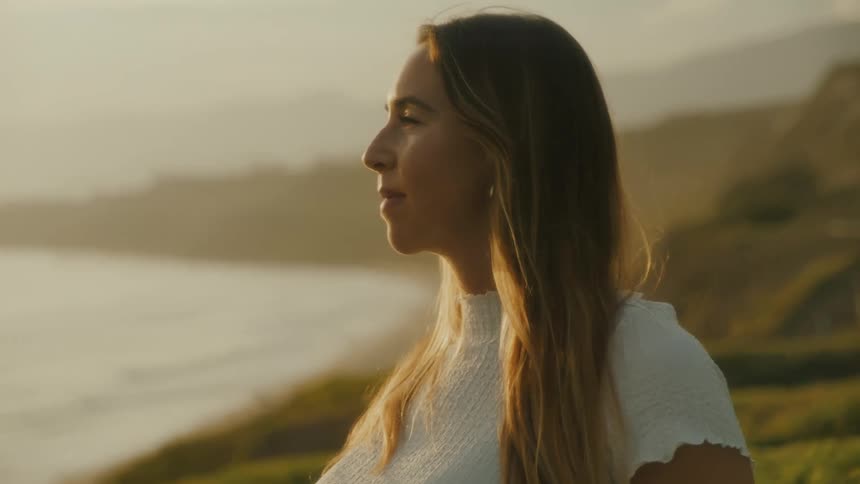 Pregnant woman watching sunset from top of hillside overlooking the ocean