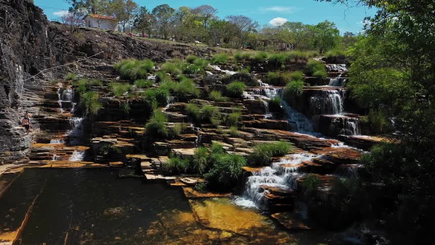 A tiered rocky waterfall flows into a clear pool amid greenery