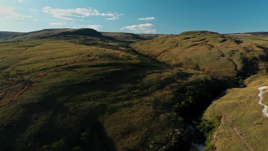 A wide aerial shot of rolling grassy hills under a clear blue sky