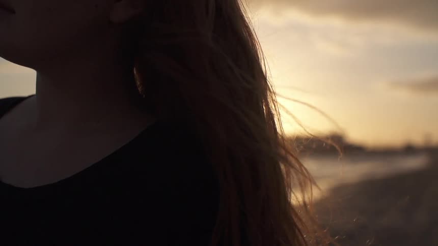 A young woman with long hair walking along a shoreline at sunset