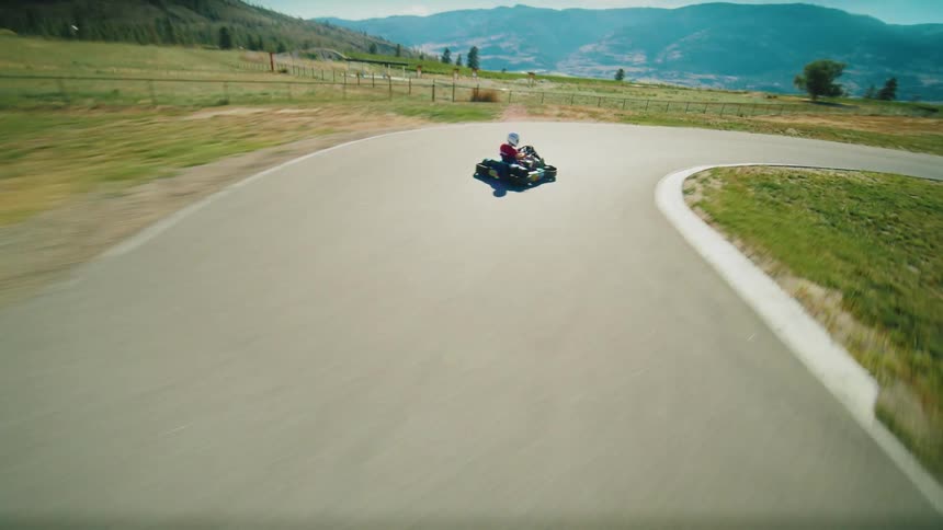 A firstperson view from a gokart shows a person on a track speeding around a right turn the scenery on both sides of the road is blurred due to the speed