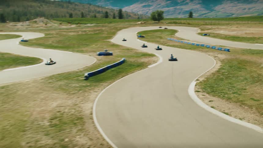 Karts races along a winding track in a field near the mountains on a summer day