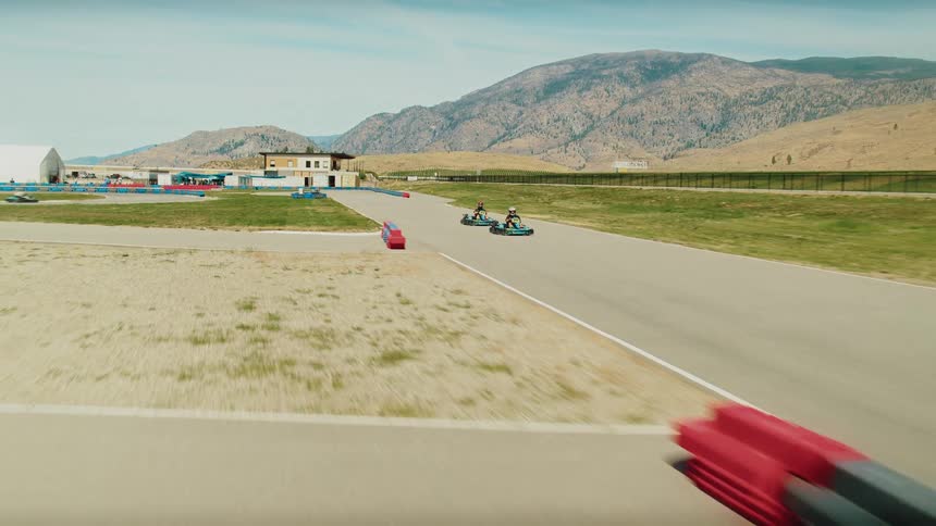 Competitors race their karts along a track in the countryside near the mountains on a cloudy day