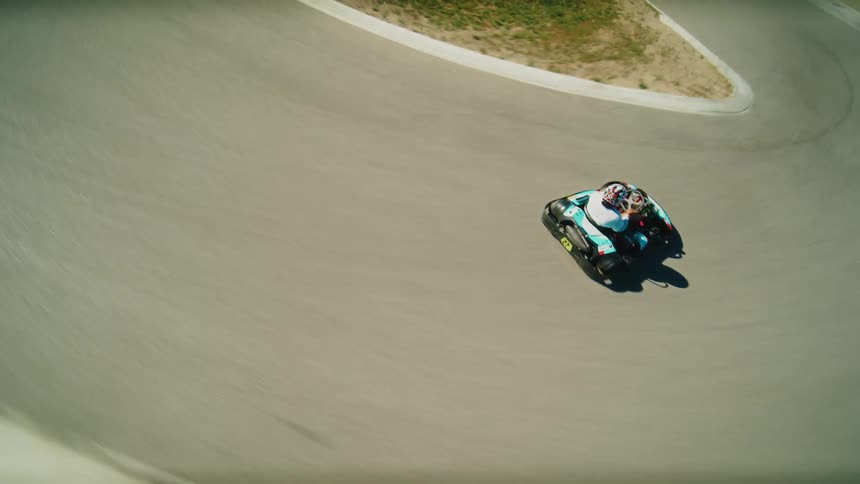 An aerial view captures a gokart speeding along a track surrounded by lush green hills the camera follows the kart as it navigates a turn