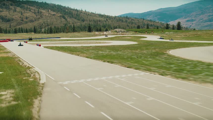 A wide aerial view shows gokarts racing on a winding track with a mountainous backdrop the camera follows the karts as they speed around the course