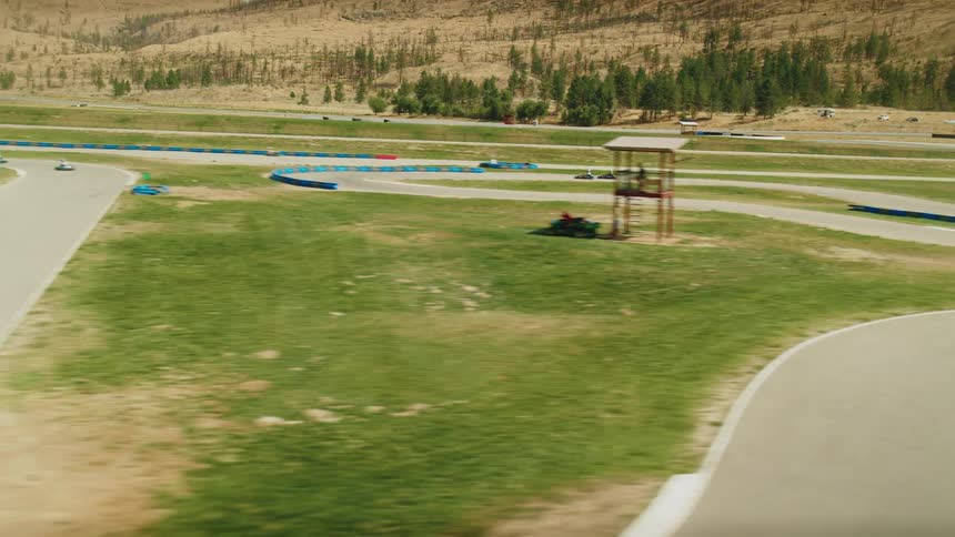 A camera films two gokarts racing on a winding track with a mountainous backdrop the video follows the gokarts as they navigate the course