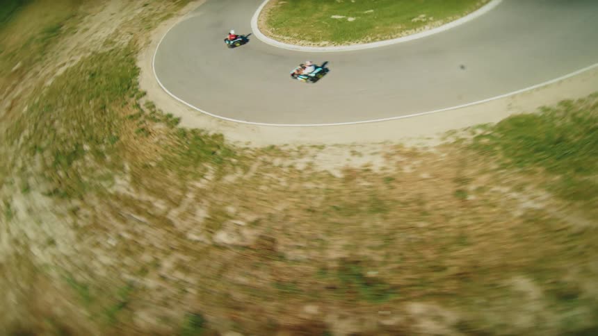 Energetic fpv drone shot of two go kart racers going around turns on the track on a bright summer day