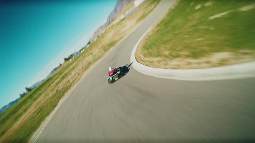 An aerial view captures a gokart speeding along a track surrounded by rolling green hills and mountains the camera follows the gokart closely as it navigates a turn