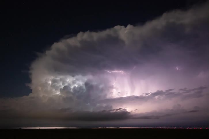 Lightning storm moves through the countryside outside a large city at night