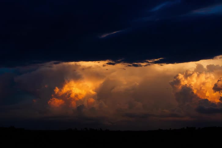 A timelapse shows dark clouds moving across a deep blue sky above the horizon with sun lit gold and orange cumulus clouds shifting beneath them