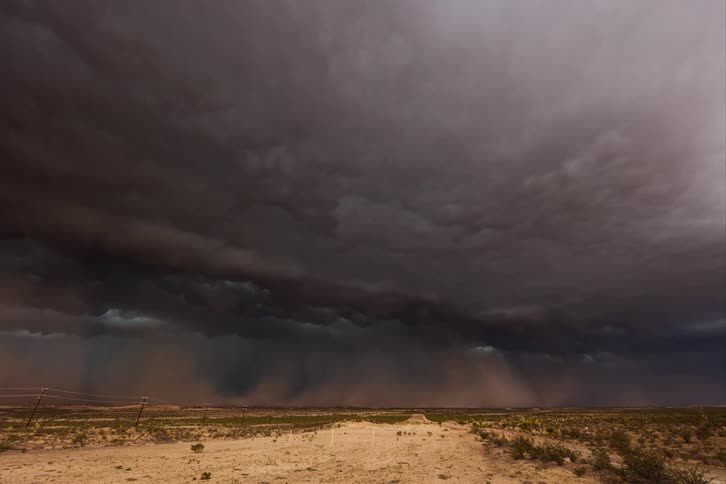 Dark storm passes over a dirt road driving dust through a pasture