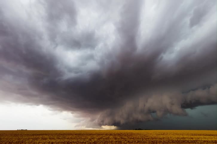 A dramatic supercell thunderstorm looms over a flat rural landscape the massive swirling cloud formation appears to be a funnel cloud extending downward toward the ground