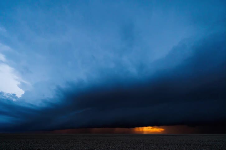 Lightning illuminates clouds in rotation moving across rural land and pouring rain
