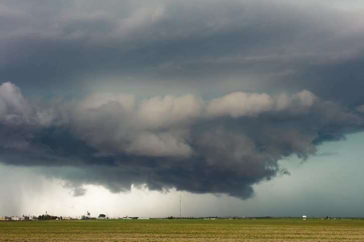 A wide shot captures a massive dark supercell storm cloud hovering over a rural landscape the cloud appears to have a large swirling base and a funnel extending downwards toward the ground