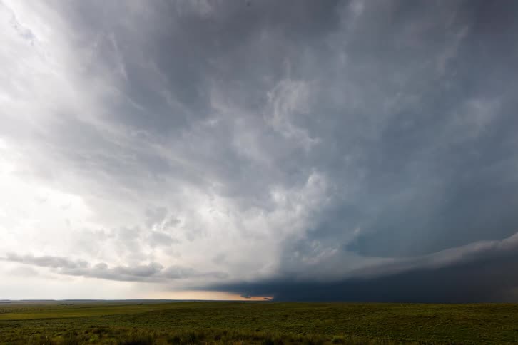 A time lapse shows a dark sprawling storm cloud moving across a field of green grass with a pale horizon