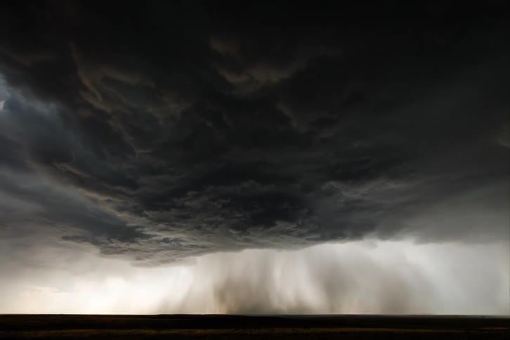 Dark storm clouds pour rain down as they move across the landscape