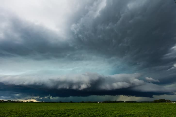 A dramatic timelapse captures a massive turbulent supercell storm cloud system forming and moving across the sky over a vast flat green field