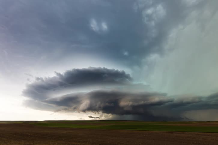 Dark heavy clouds moving on the sky over a flat field covered in grass during dusk or dawn