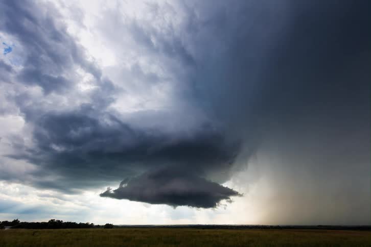 A time lapse shows large gray clouds moving above a grassy plain