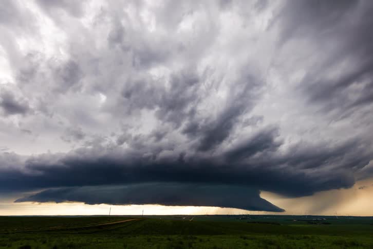 Sunlight shines underneath dark storm clouds rolling over a grassy field