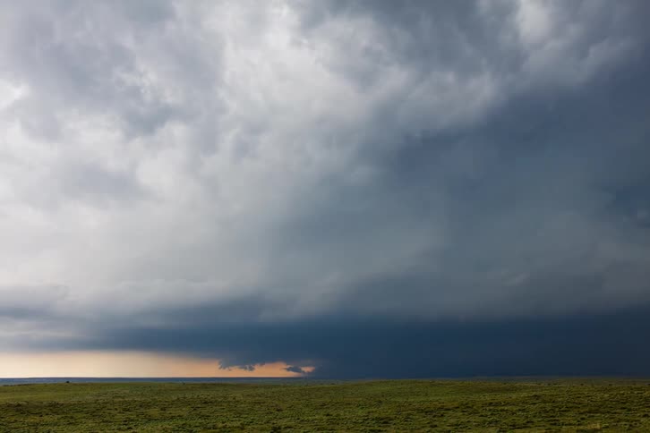 A dark storm looms over the plains under the sunset