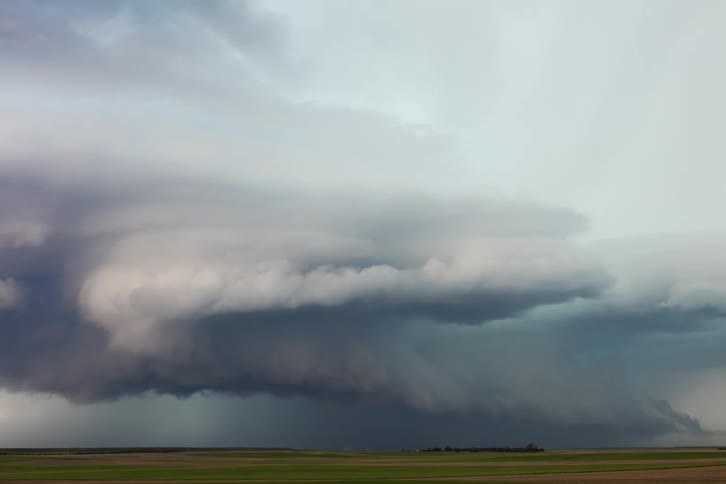 Dark swirling storm clouds dominate the sky over a flat farmland landscape