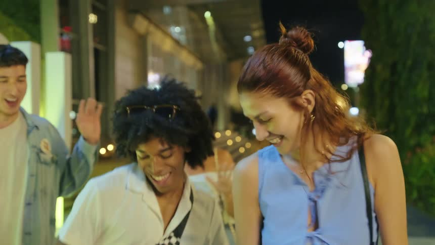 Friends laugh and dance while walking a lit city sidewalk