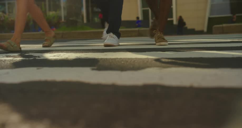 A lowangle groundlevel shot focuses on a crosswalk as the outoffocus feet of several pedestrians walk across the street