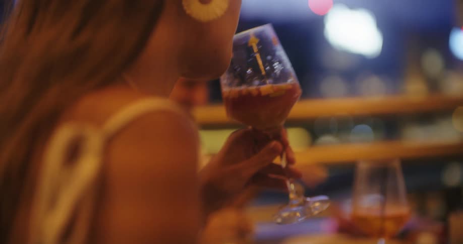 Woman drinks a cocktail glass in a brightly lit nighttime setting