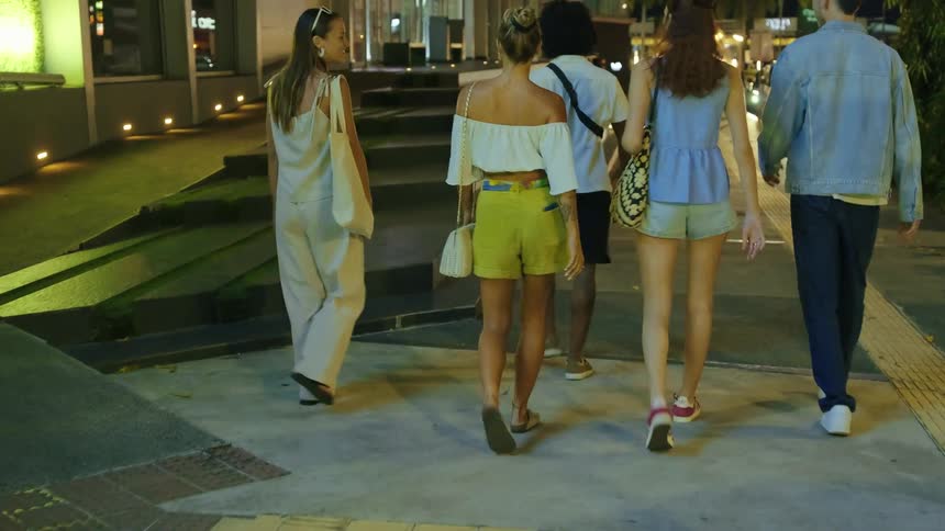 Young friends walk together on a city sidewalk at night