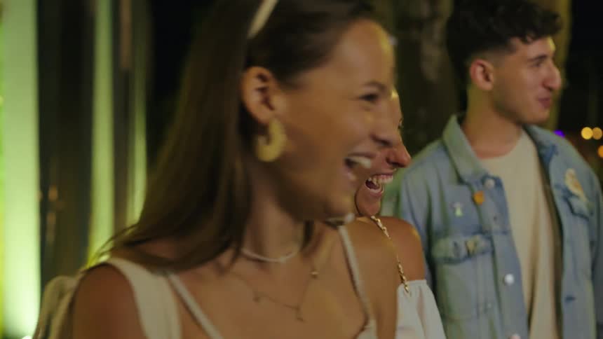 Friends laugh and chat together on a city street at night