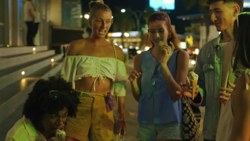 The video shows a group of friends walking and laughing together at night on a city street they are holding ice cream cones and appear to be enjoying their time together as they socialize