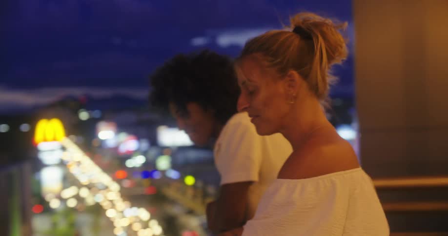 Couple smiles on a balcony overlooking the city lights at night