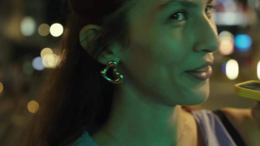 Longhaired woman smiling while talking on a smart phone held in her hand outdoors during night time in a metropolitan area