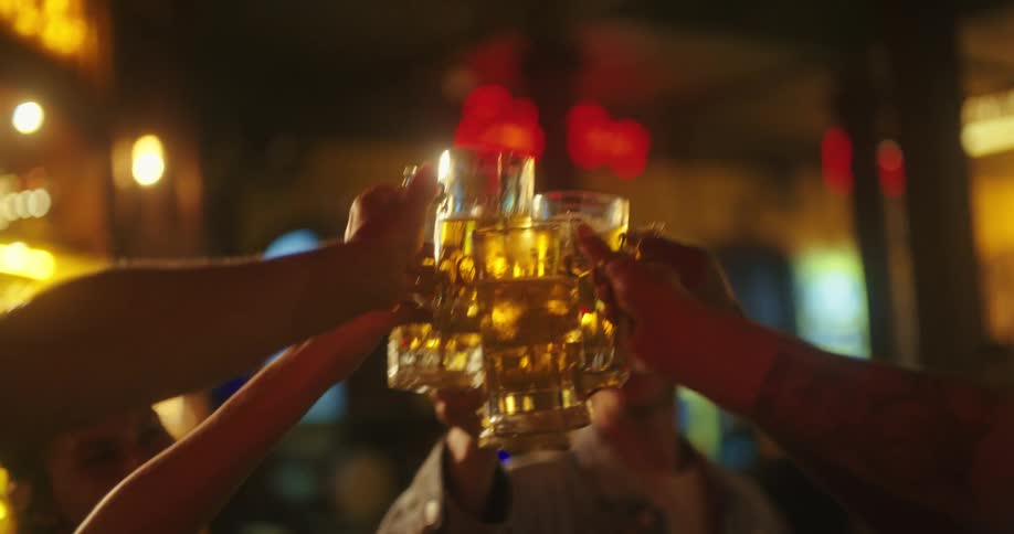 A group of people smile as they all raise their beer mugs and touch them together