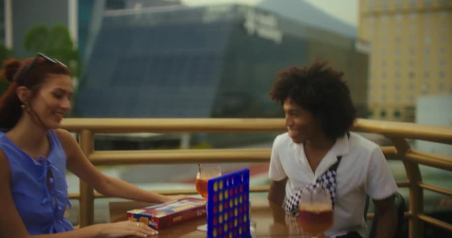 A group of happy friends is gathered at a table on a rooftop patio celebrating and highfiving while enjoying a game