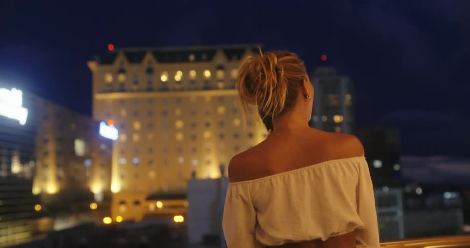 A woman talks on her phone while standing on a balcony at night