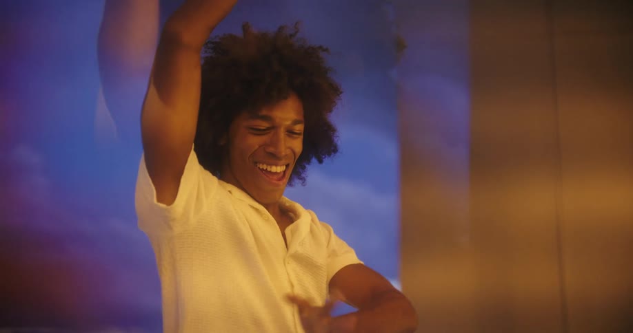 Woman watches a smiling man dance on a balcony overlooking a busy freeway at night