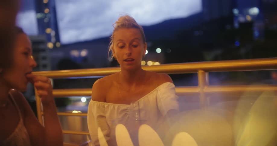 A group of young woman converse on a balcony while eating food