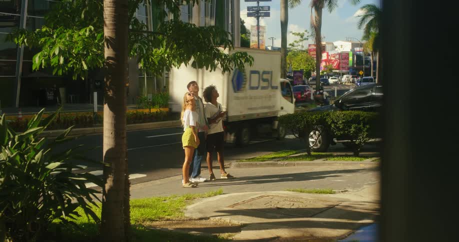 Three people wave excitedly on an urban sidewalk