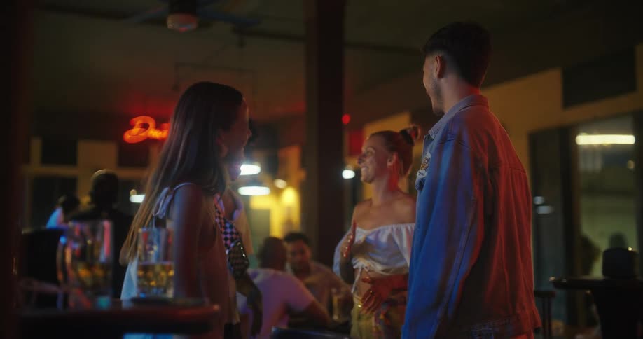 Group of young people chatting in a bar lit with colorful lights
