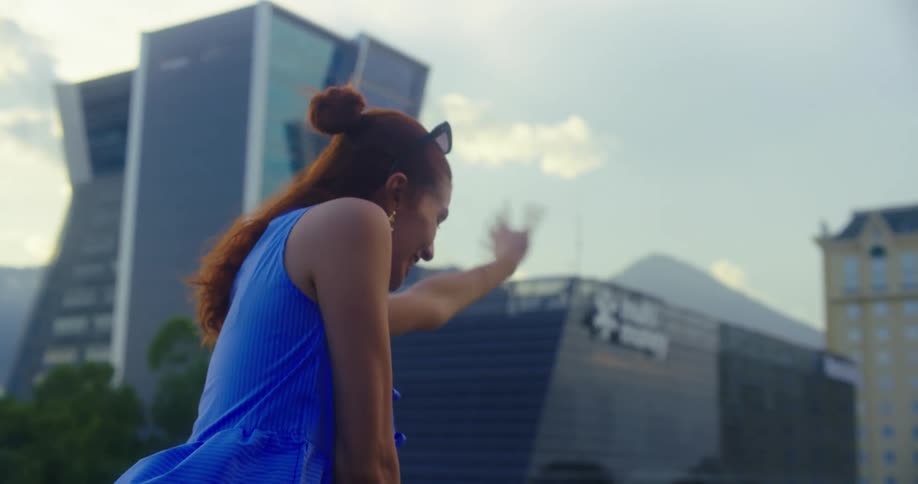 Woman standing on a balcony in the city waves to someone below on a cloudy summer day