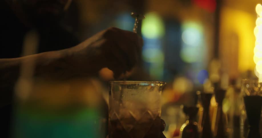 Male bartender mixes a drink before pouring it through a strainer onto ice