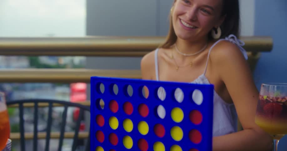 A young woman sitting on the balcony of a highrise building playing a game at a table