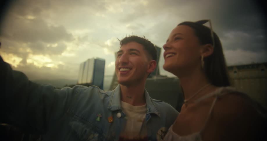 A couple video calls on a rooftop with city buildings behind