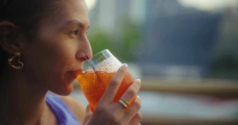 A woman sips a cold orange drink through a straw outdoors