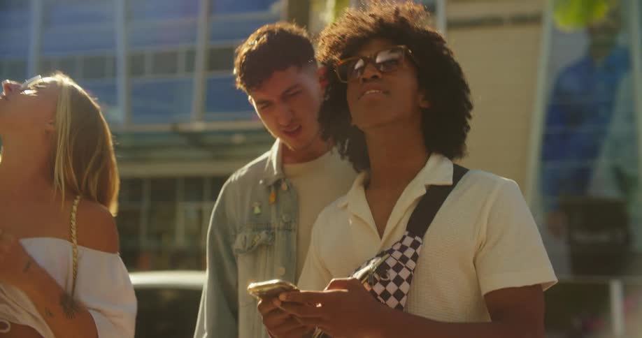 Three friends walk together on a sidewalk smiling as they look at a smartphone searching for an adress