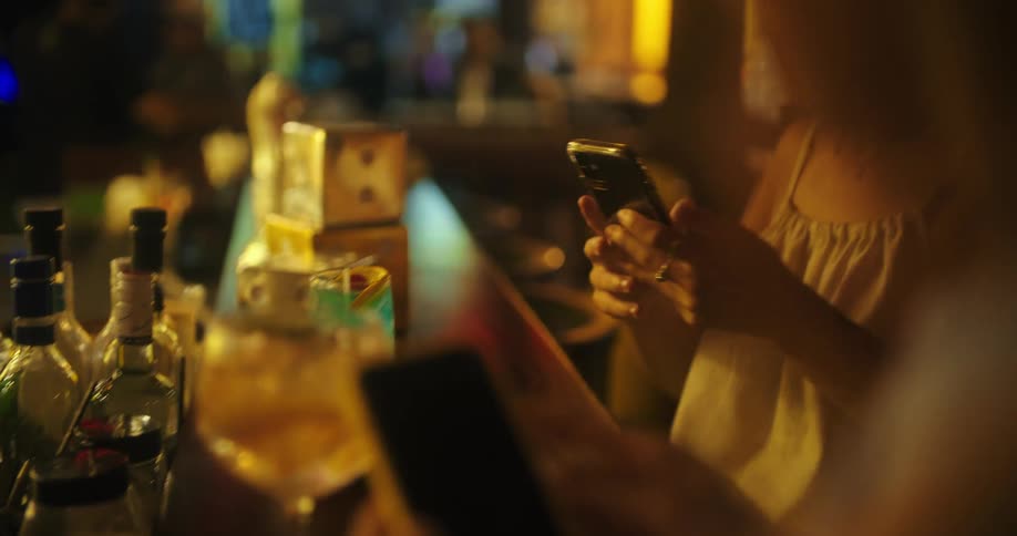Person captures drink glass with phone in a dimly lit bar