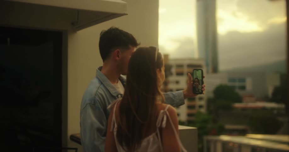 Couple hugging on a balcony making a video call at sunset
