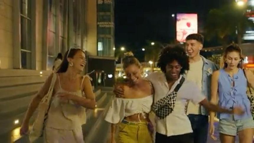 The video shows a group of young adults walking away from a building with a large american express sign the people are laughing and smiling as they walk down the street at night